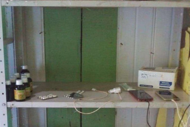 foto de uma prateleira de metal em que há alguns poucos frascos de remédio, carregadores e dois celulares