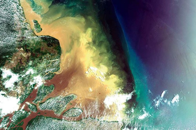 Imagem mostra visão via satélite da foz do Rio Amazonas, com a costa verde à esquerda e águas marrons e esverdeadas se misturando com o oceano azul-escuro à direita.