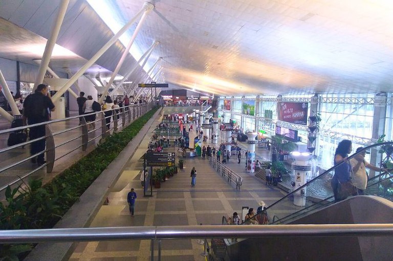 Foto interna e ampla do Aeroporto Internacional de Belém, mostrando pessoas em rampas, escadas rolantes e saguão com arquitetura moderna e teto inclinado.