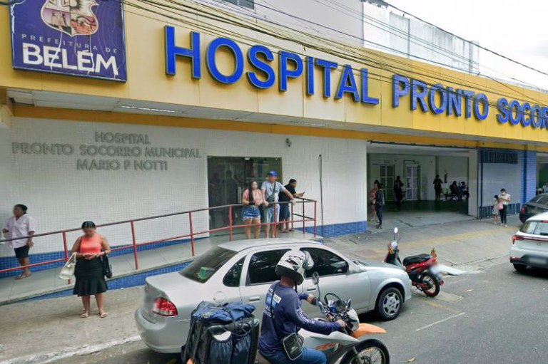 Fachada amarela com letreiro azul "Hospital Pronto-Socorro" e logo da Prefeitura de Belém. Pessoas estão na rampa e veículos transitam na rua à frente.