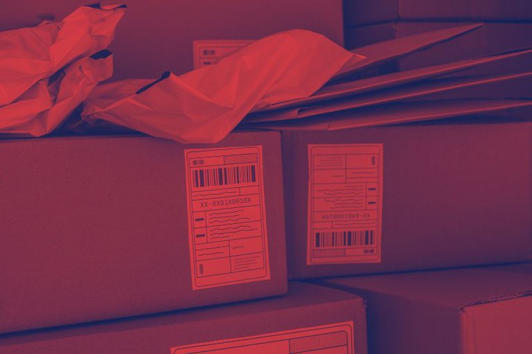 Fotografia com forte tonalidade avermelhada/magenta. Mostra caixas de papelão empilhadas, com etiquetas de envio (contendo códigos de barras e espaço para texto) visíveis. Sobre as caixas, há embalagens plásticas e envelopes, alguns amassados.