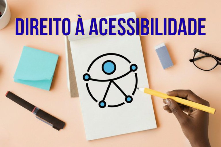 Mão segura lápis sobre caderno com símbolo da acessibilidade entre itens de escritório. Texto: Direito à acessibilidade