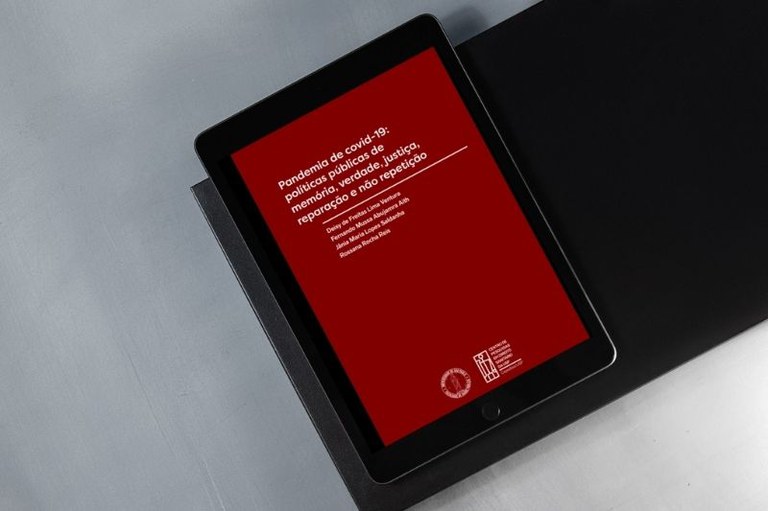 Tablet sobre superfície cinza exibe capa de livro vermelha com título Pandemia de covid-19 e nomes de autores em branco.