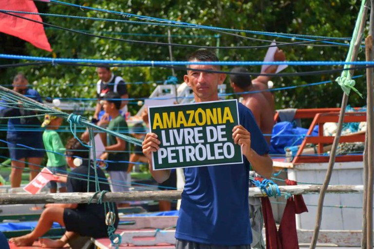 Homem de camiseta azul segura cartaz verde com os dizeres 'Amazônia Livre de Petróleo' em letras amarelas e brancas