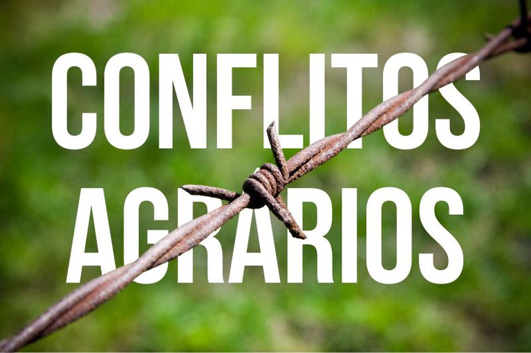 Sobre fundo verde desfocado, arame farpado enferrujado cruza a imagem na diagonal. Texto branco em caixa alta ao centro: Conflitos agrários.