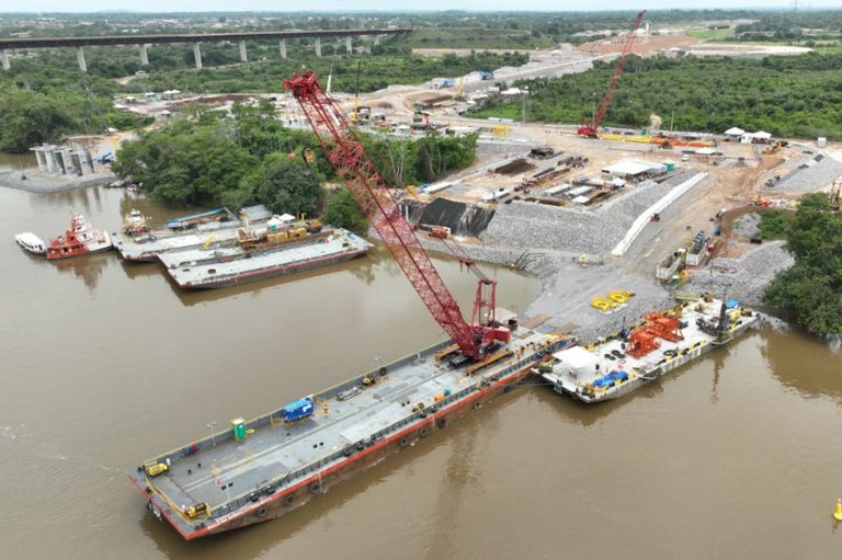 Grande canteiro de obras com um guindaste em uma balsa em no Rio Tocantins, com uma ponte ao fundo