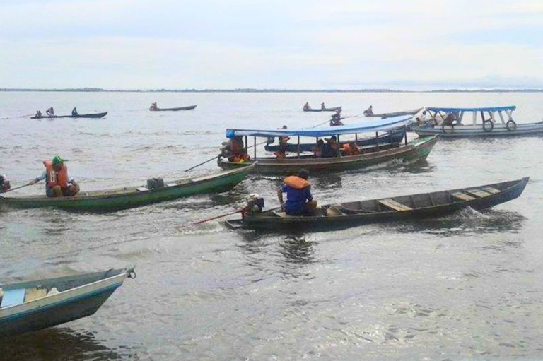 Inclua a descrição de acessibilidade: foto de várias embarcações pequenas navegando em um corpo d'água. Algumas pessoas estão usando coletes salva-vidas laranja. O céu está nublado e a água tem uma aparência calma.