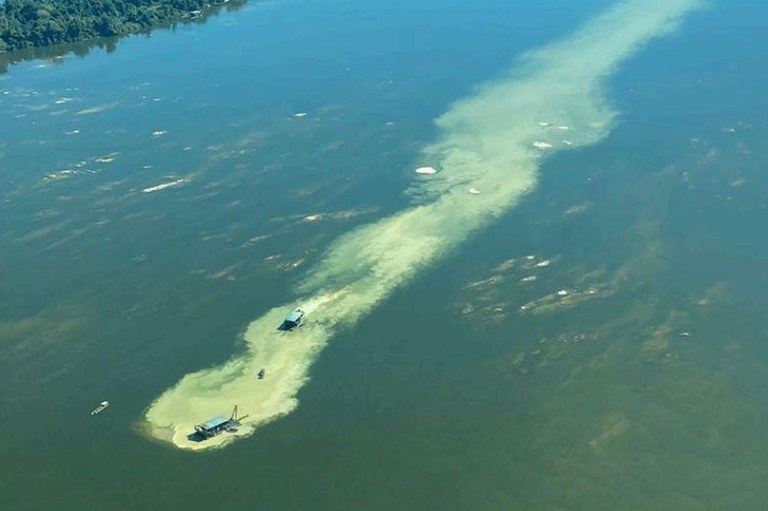 Foto aérea de um rio. No centro, duas dragas emitem uma extensa nuvem de sedimentos na água escura.