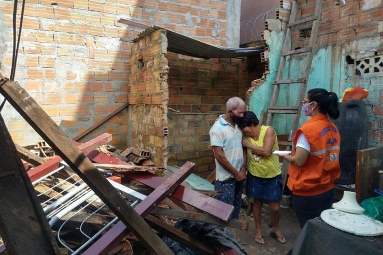 Entre destroços e paredes de tijolos, casal se abraça enquanto mulher com colete da Defesa Civil de Belém faz anotações em bloco.