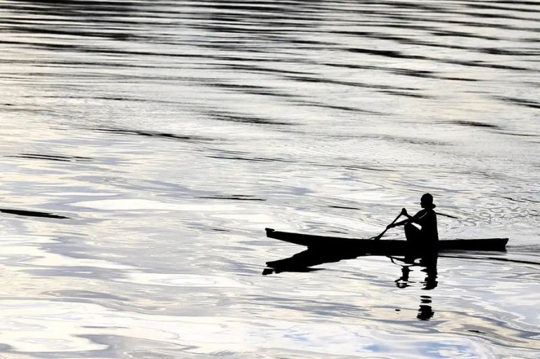 Silhueta de uma pessoa remando uma canoa em águas onduladas.