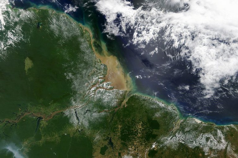 Imagem satélite da Foz do Rio Amazonas no Oceano Atlântico, com terra verde à esquerda, águas marrons encontrando o oceano azul e nuvens à direita