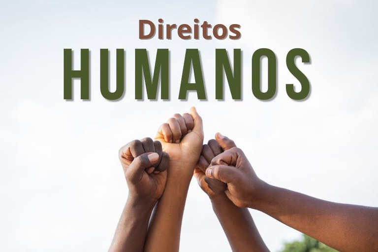 Foto de quatro mãos de diferentes etnias e tonalidades erguidas, com os punhos cerrados e unidos. Acima, o texto “Direitos Humanos”.