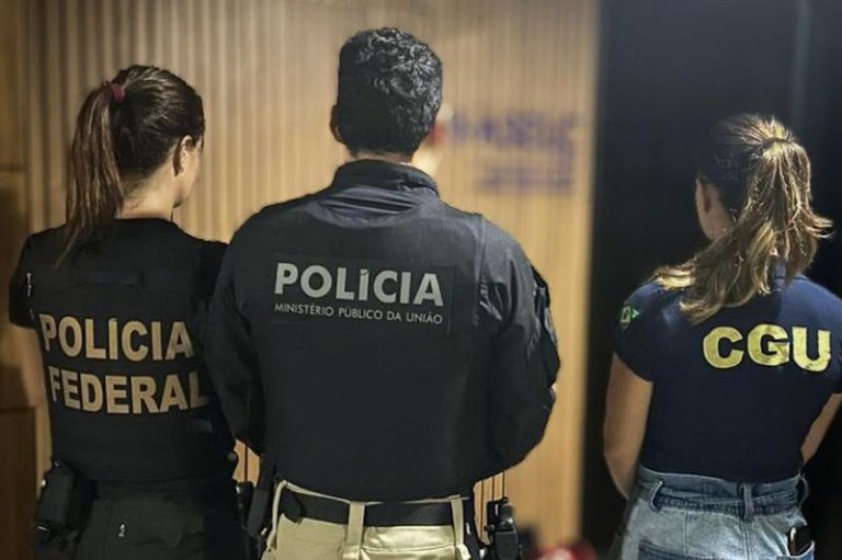 Três agentes de costas, lado a lado, com uniformes da Policia Federal, Policia do Ministério Público da União e CGU