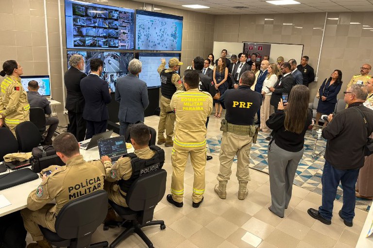 Foto mostra profissionais reunidos em uma sala de controle olhando para um telão