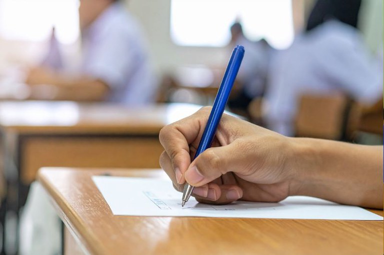 Foto em detalhe de um candidato com uma caneta azul na mão fazendo prova