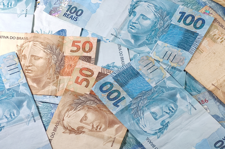 Foto mostra diversas cédulas de 50 e 100 reais dispostas de forma desorganizada