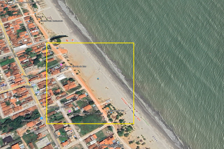 Fotografia aérea da Praia Central de Lucena (PB), com casas e construções à direita e a faixa de areia e o mar à esquerda. Há um quadrado vazado com bordas amarelas delimitando uma área da faixa de areia, no centro da imagem.