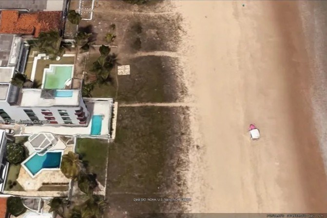 Imagem aérea de área costeira em João Pessoa mostra edifícios residenciais com piscinas cercados por vegetação, à esquerda; faixa de areia ampla e mar com diferentes tons de azul, à direita. Há uma estrutura pequena próxima à praia e o endereço "Gov. Argemiro de Figueiredo, 1298, Jardim Oceania" está indicado.