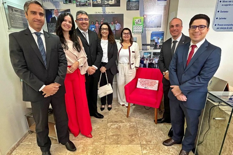 Foto mostra sete pessoas na foto posando ao lado do banco vermelho