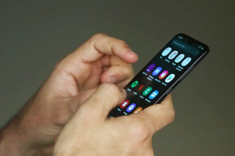 A imagem mostra uma pessoa segurando e utilizando um smartphone com as duas mãos.