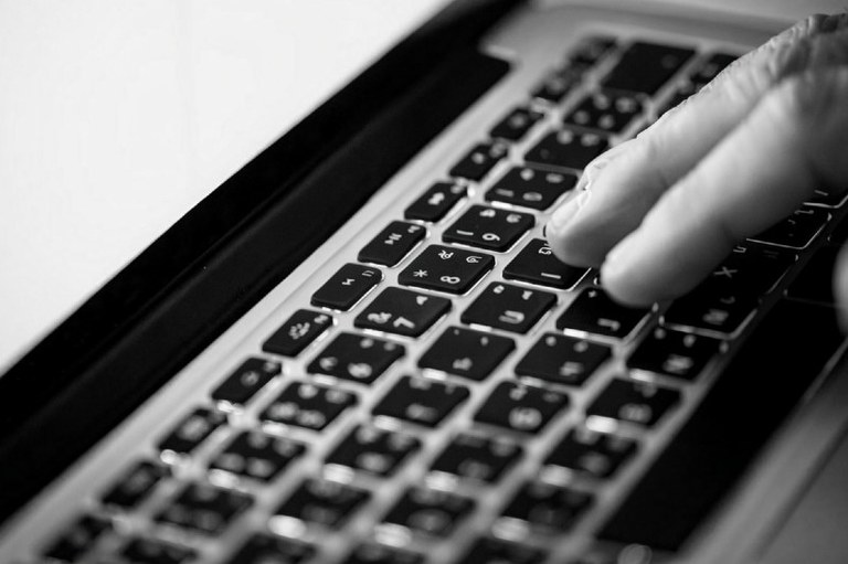 Foto em preto e branco mostra uma mão no teclado de um computador