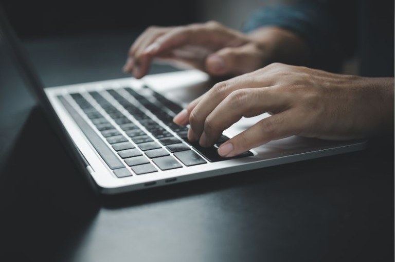 Imagem em detalhe de um homem digitando em um teclado de notebook