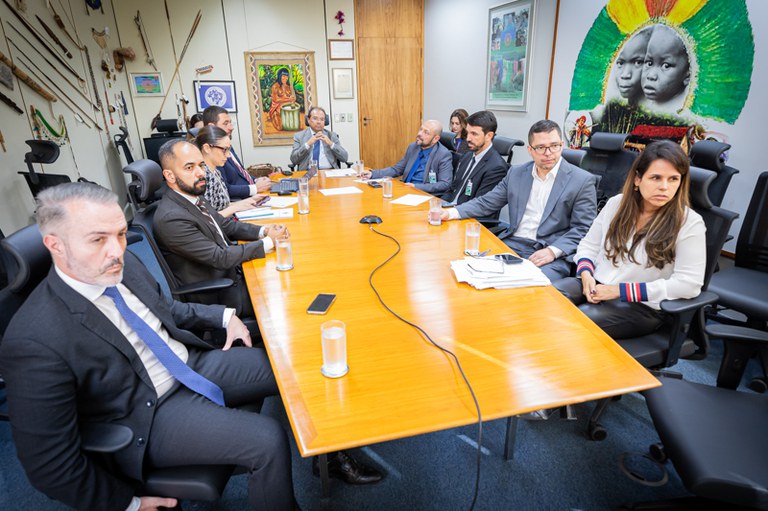 Imagem mostra homens e mulheres sentados ao redor de mesa de reuniões.
