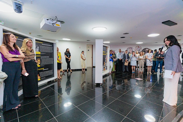 Imagem mostra mulher falando ao microfone para o público presente na exposição