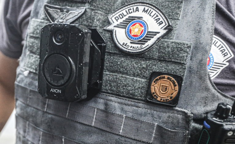 Imagem mostra parte do uniforme de um policial militar com uma câmera corporal fixada no colete.