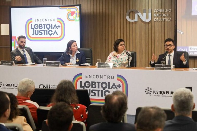 Imagem mostra quatro pessoas sentadas atrás de bancada de auditório.