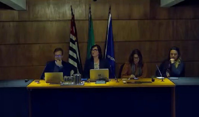 Imagem mostra quatro pessoas sentadas atrás de uma bancada.