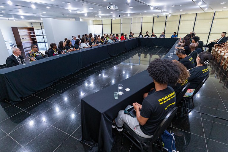 Imagem mostra mais de 30 pessoas, entre homens e mulheres, sentadas em volta de mesa de reunião.