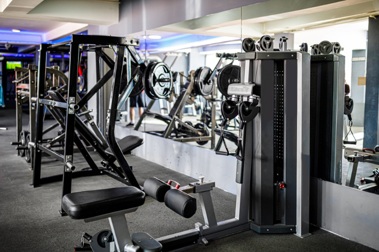 Imagem de uma academia de ginástica com vários equipamentos para exercícios físicos.