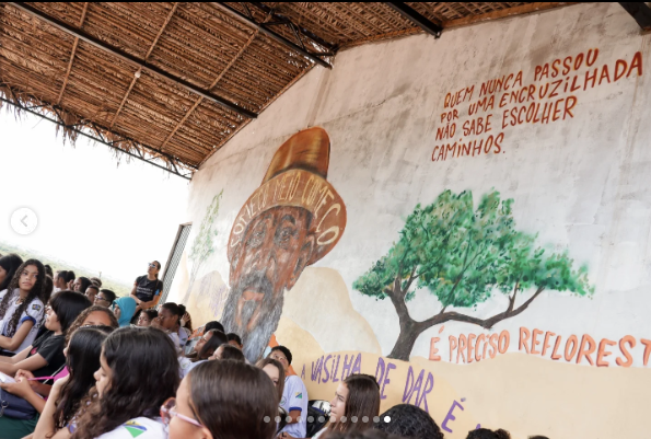 Foto mostra um painel de líder quilombola na parede e alunos em volta