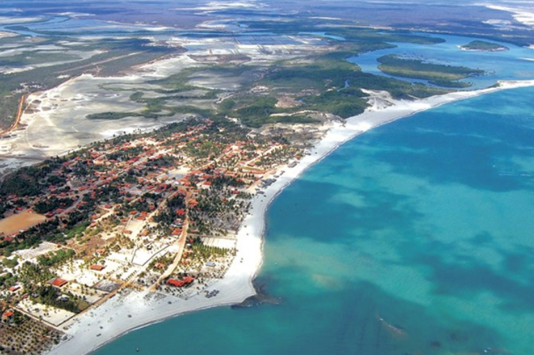 Vista aérea da cidade de Cajueiro da Praia, no Piauí, mostrando a orla com casas e vegetação. Do lado esquerdo, é possível ver um rio e manguezais e, à direita, o mar com águas azuis.