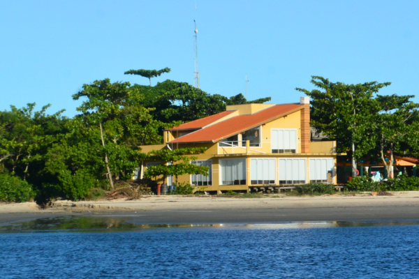 Foto mostra uma casa de veraneio na cor amarela construída em frente à praia