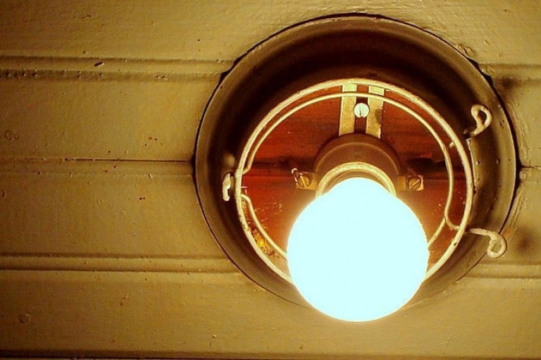 Lâmpada acesa em um teto de madeira. O foco está no brilho da luz, indicando um ambiente interno iluminado.