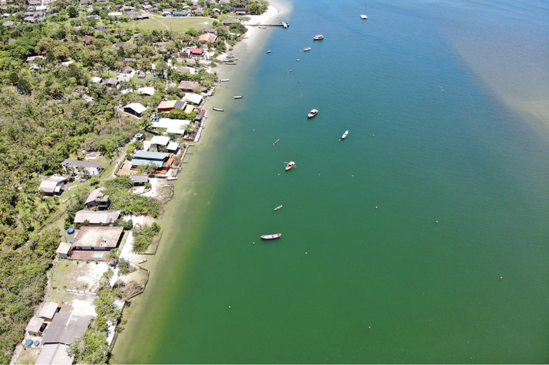 Imagem aérea da Ilha das Peças, no litoral do Paraná, mostrando área costeira com casas próximas à margem e vegetação nativa ao redor.