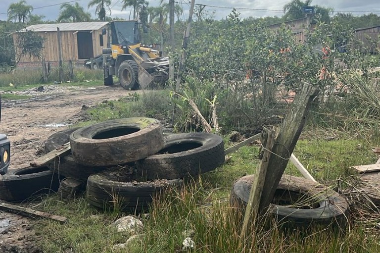 Foto mostra pneus descartados. Ao fundo uma retroescavadeira