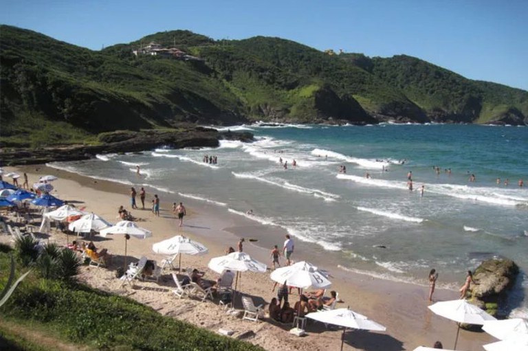 Foto mostra praia com águas esverdeadas e guardas-sol na areia