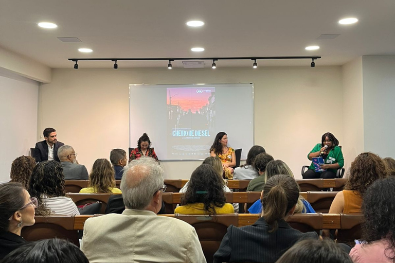 Foto mostra debatedores sentados e o cartaz do filme logo atrás