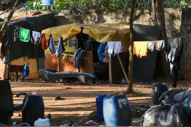 Foto mostra acampamento de pessoas em situação de rua com barracos e roupas em varal