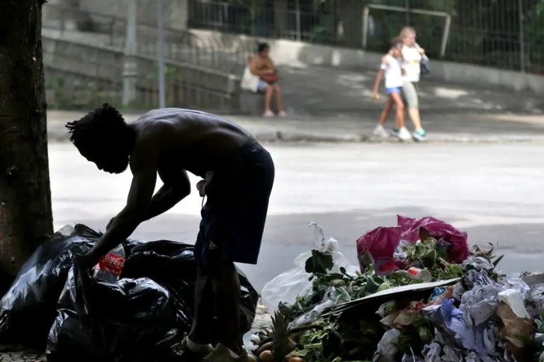 Foto mostra uma pessoa em situação de rua vasculhando o lixo