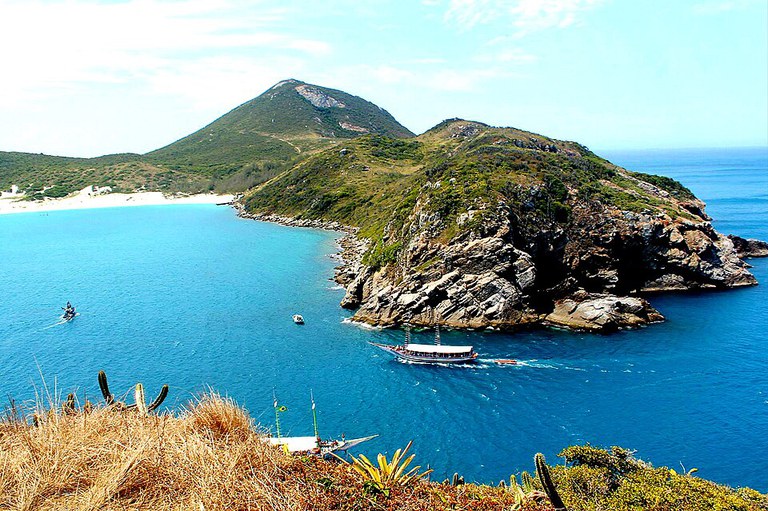 Vista panorâmica de Arraial do Cabo com águas azul-turquesa, barcos navegando e morros com vegetação ao fundo