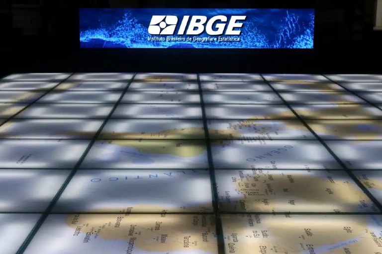 Foto mostra a logo do IBGE sobre um mapa mundi