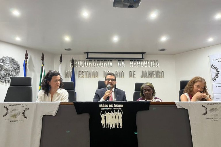 Foto mostra mesa do evento com 4 pessoas, sendo três mulheres e o procurador regional dos Direitos do Cidadão adjunto ao centro falando ao microfone