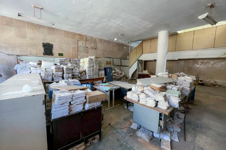 Foto mostra documentos em mal estado de conservação, em um ambiente improvisado