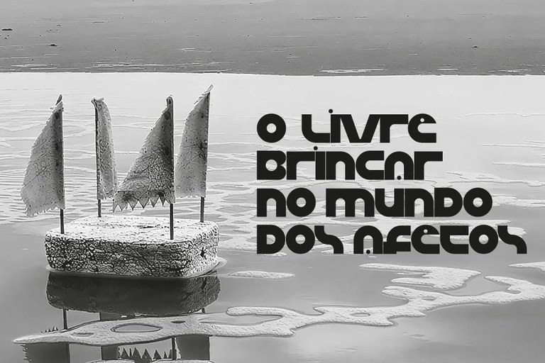 Fotografia horizontal em preto e branco. À esquerda, um pequeno barco artesanal flutua sobre água calma, projetando reflexo nítido. A embarcação é composta por uma base retangular de textura porosa, assemelhando-se a isopor ou pedra-pomes, com quatro mastros finos que sustentam velas triangulares de tecido rústico. À direita, o texto em letras pretas e arredondadas diz: "o livre brincar no mundo dos afetos". O fundo apresenta uma linha de horizonte suave com margem de areia e água rasa.