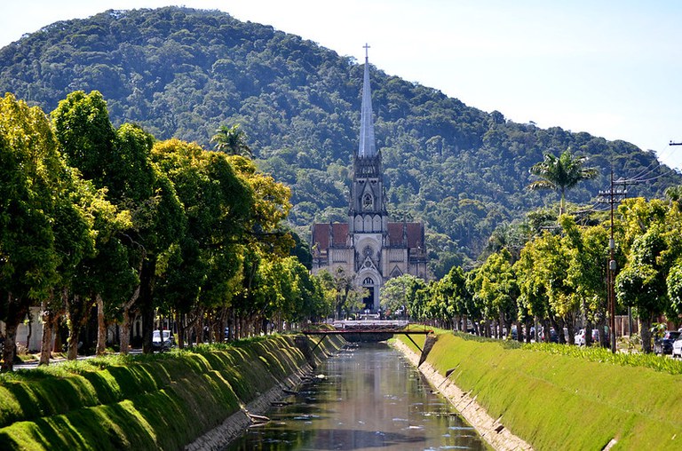 Foto mostra Catedral de Petrópolis ao fundo e caminhos de árvores nas margens de canal em primeiro plano