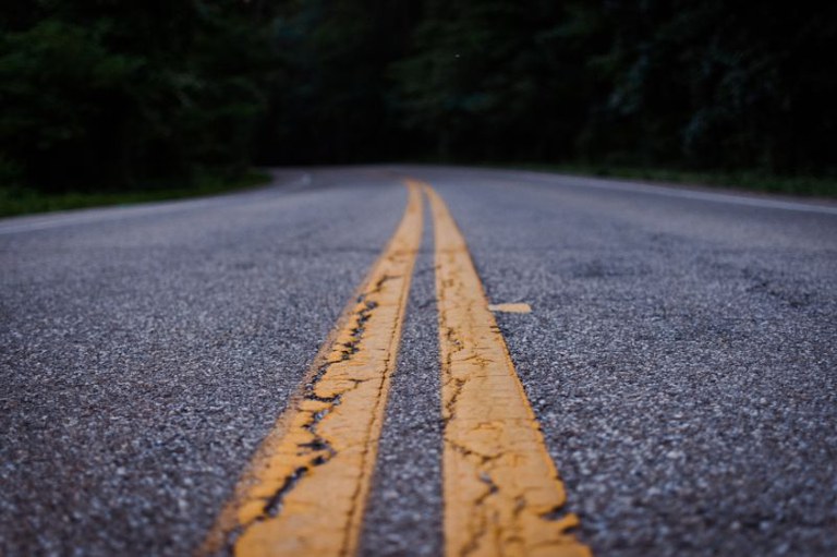imagem do asfalto de uma estrada com a faixa amarela que divide as pistas